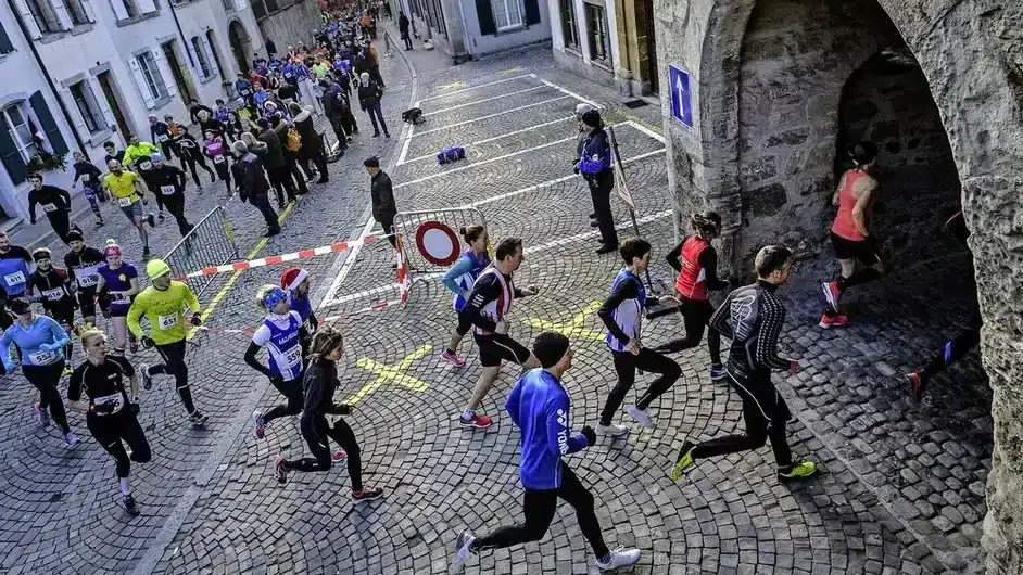 Coureurs de tous âges participant à la Coupe de Noël à Estavayer, naviguant à travers les rues pavées et sous les arches médiévales, avec des spectateurs les encourageant depuis le bord de la route, capturant l'esprit communautaire de la course