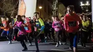 Jeunes coureurs enthousiastes prenant un départ rapide lors d'une course nocturne à Avenches, éclairés par les lumières de la ville et encouragés par les spectateurs, capturant l'énergie et l'excitation de l'événement sportif