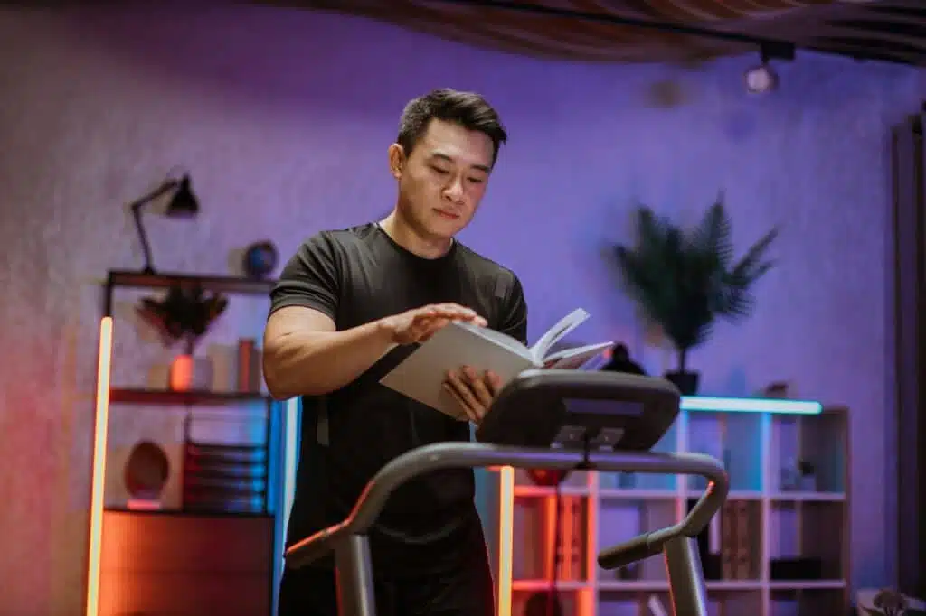 Attractive young sports asian man reading book while doing fitness exercise, running on treadmill